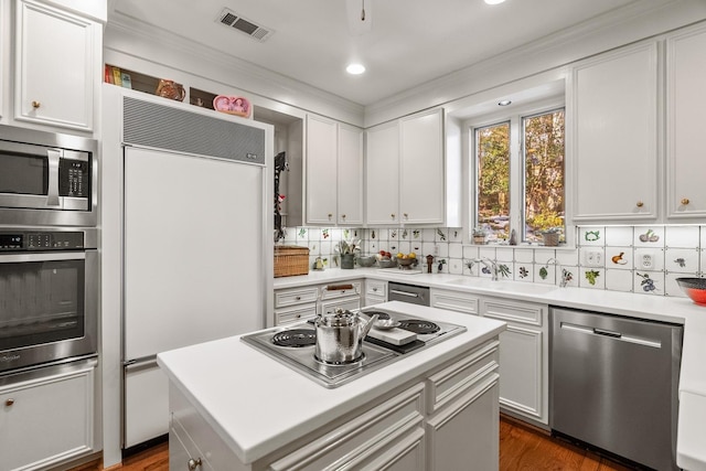 kitchen featuring sink, white cabinetry, a center island, built in appliances, and decorative backsplash