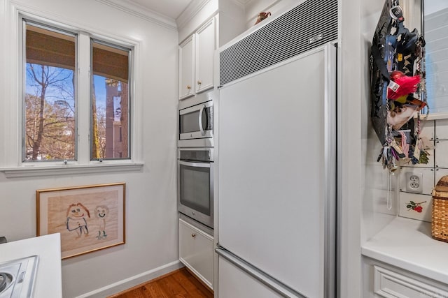 kitchen with ornamental molding, appliances with stainless steel finishes, white cabinets, and light wood-type flooring