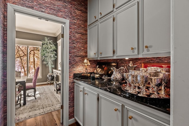 bar with crown molding, dark stone counters, and hardwood / wood-style floors