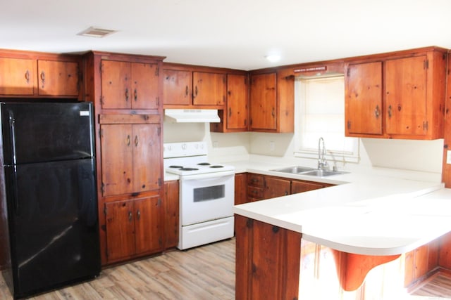 kitchen featuring a kitchen bar, white electric range oven, black fridge, light hardwood / wood-style flooring, and kitchen peninsula