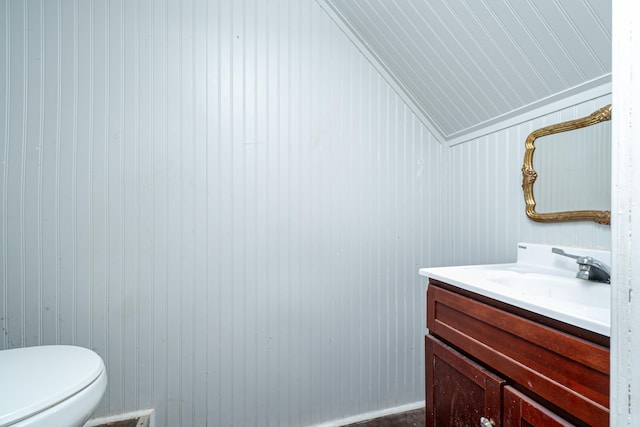 bathroom with vanity, vaulted ceiling, wooden walls, and toilet