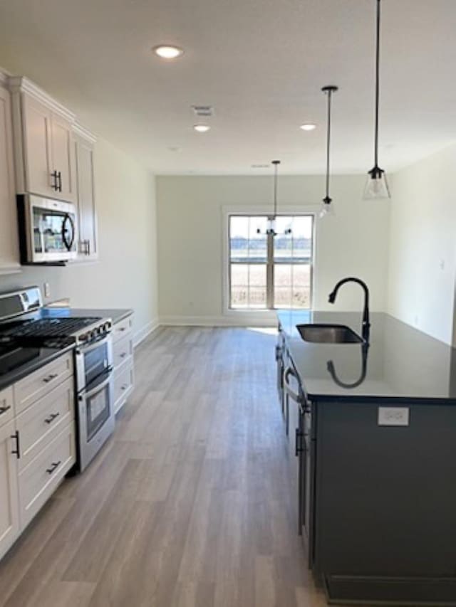 kitchen with appliances with stainless steel finishes, pendant lighting, sink, white cabinets, and a center island with sink