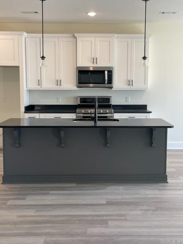 kitchen featuring white cabinetry, decorative light fixtures, stainless steel appliances, and light wood-type flooring