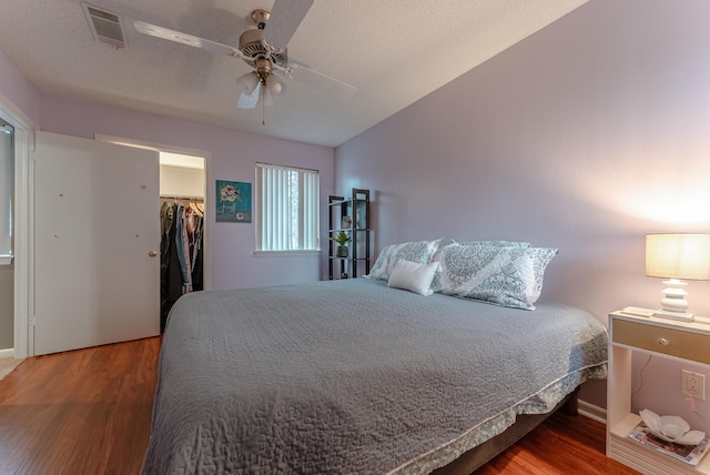 bedroom with a spacious closet, a textured ceiling, a closet, hardwood / wood-style flooring, and ceiling fan