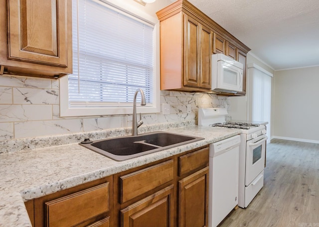 kitchen with sink, light stone counters, light hardwood / wood-style flooring, white appliances, and backsplash