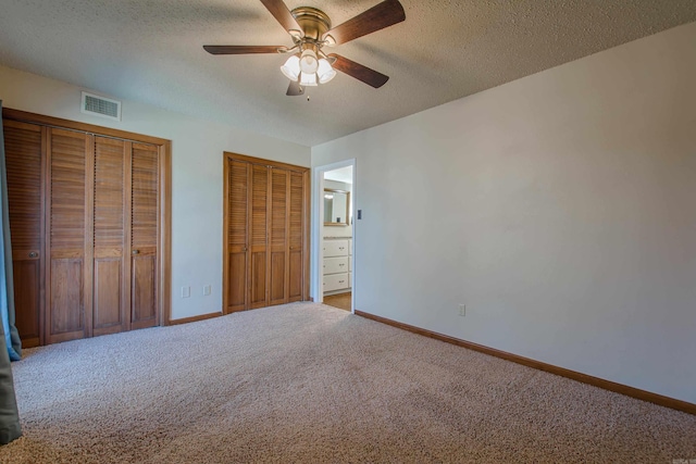 unfurnished bedroom featuring carpet floors, two closets, a textured ceiling, and ceiling fan