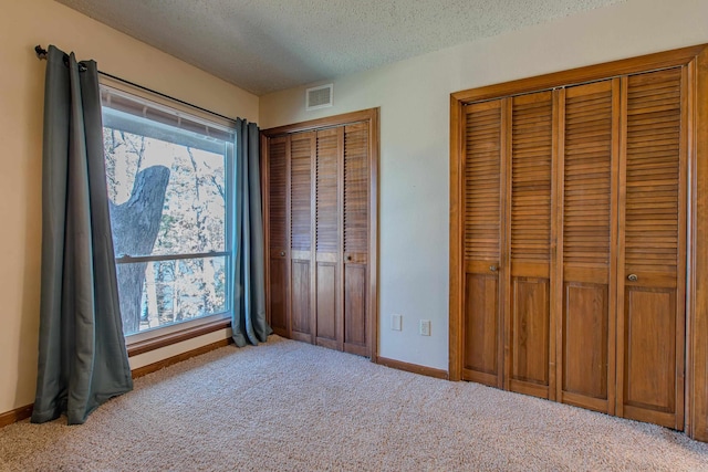 unfurnished bedroom with multiple closets, light carpet, and a textured ceiling