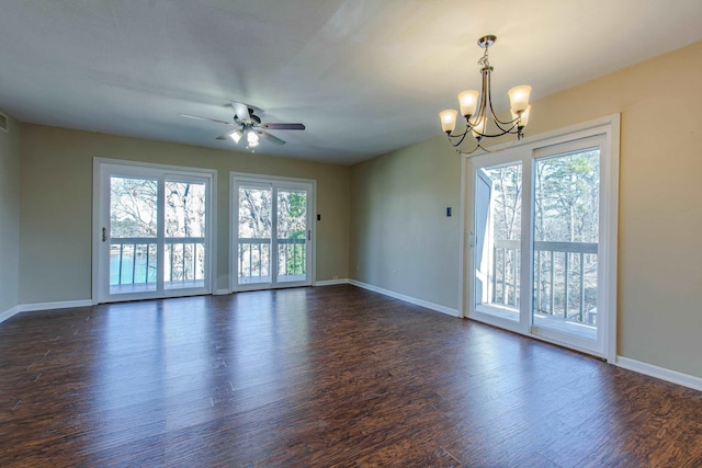 empty room featuring dark hardwood / wood-style floors, ceiling fan with notable chandelier, and a wealth of natural light