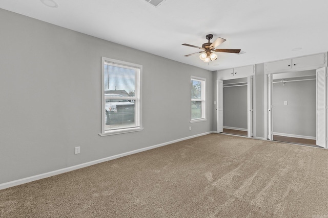 unfurnished bedroom featuring ceiling fan, carpet floors, and two closets