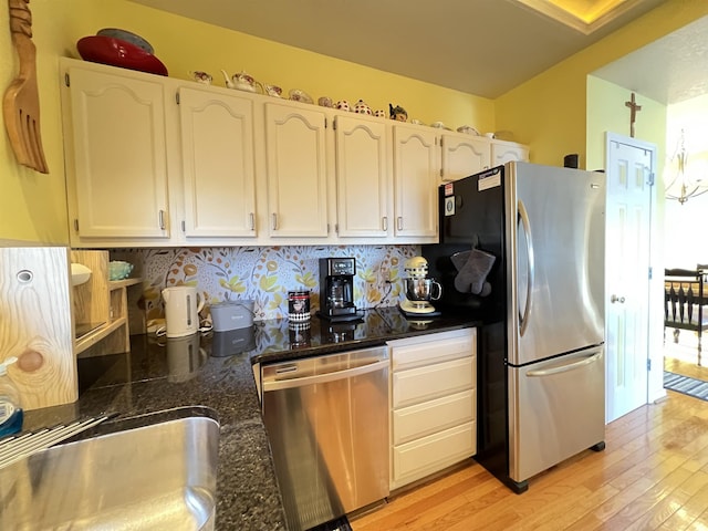 kitchen with appliances with stainless steel finishes, white cabinetry, backsplash, dark stone countertops, and light hardwood / wood-style floors