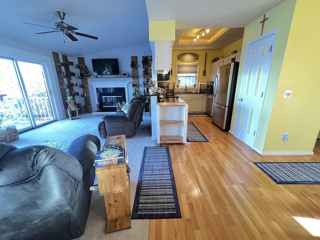 living room with ceiling fan, a healthy amount of sunlight, a raised ceiling, and light hardwood / wood-style flooring