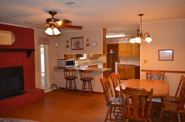 dining area with sink, hardwood / wood-style flooring, ornamental molding, a brick fireplace, and ceiling fan with notable chandelier