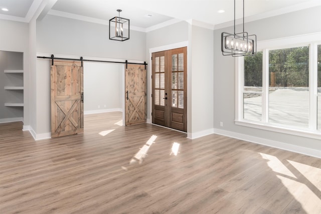 unfurnished dining area featuring crown molding, a barn door, light hardwood / wood-style flooring, and a notable chandelier