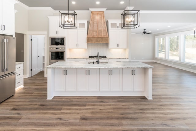 kitchen featuring a kitchen island with sink, hanging light fixtures, stainless steel appliances, and white cabinets