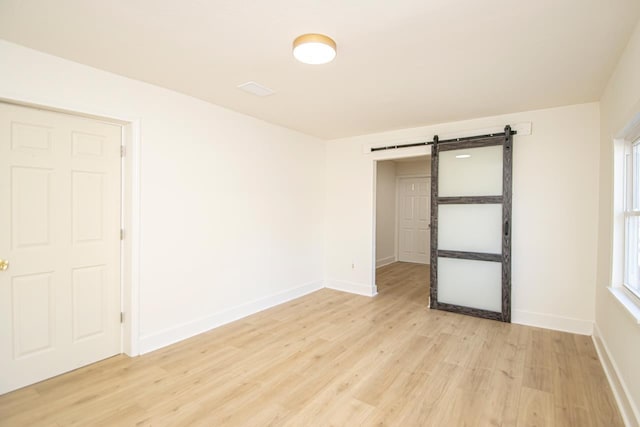 unfurnished bedroom with a barn door and light wood-type flooring