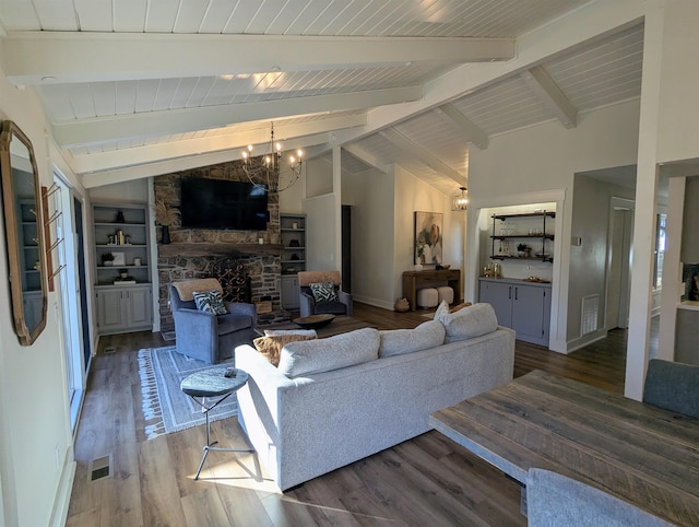 living room with a stone fireplace, lofted ceiling with beams, wood-type flooring, a notable chandelier, and built in shelves