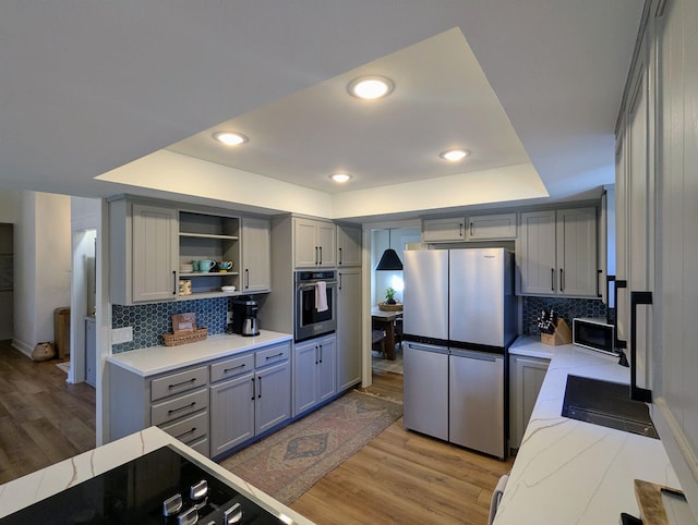 kitchen featuring appliances with stainless steel finishes, a tray ceiling, light wood-type flooring, and gray cabinetry