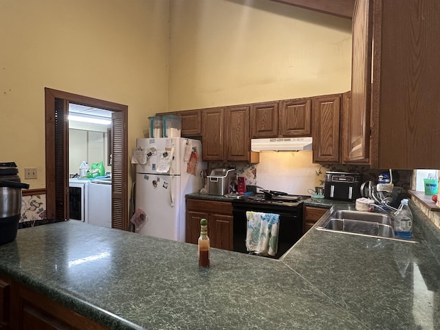 kitchen featuring washer and dryer, a towering ceiling, black electric range oven, sink, and white fridge