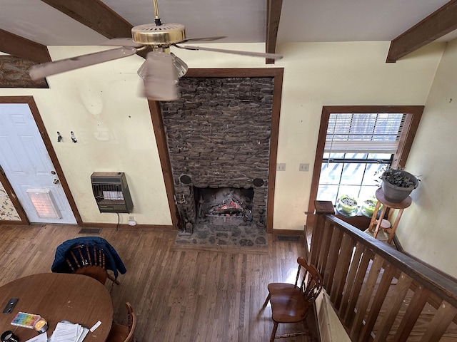 living room with a stone fireplace, heating unit, beamed ceiling, ceiling fan, and hardwood / wood-style floors