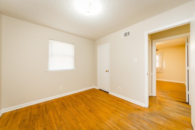 unfurnished room with a textured ceiling and light wood-type flooring