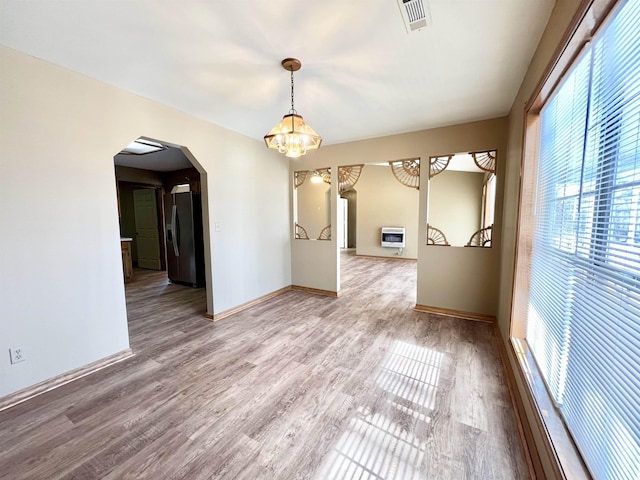 empty room featuring wood-type flooring, a chandelier, and heating unit