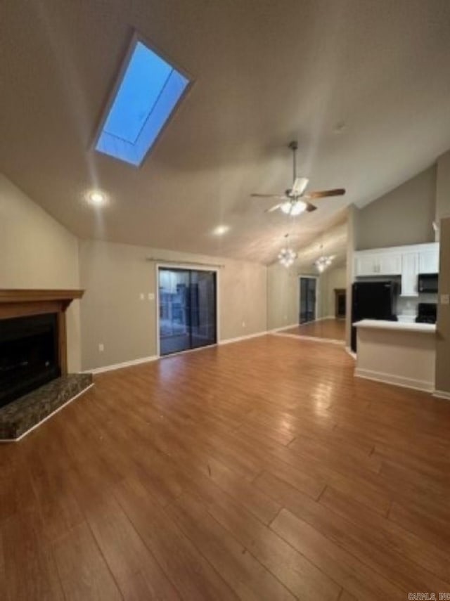 unfurnished living room featuring wood-type flooring, vaulted ceiling with skylight, and ceiling fan