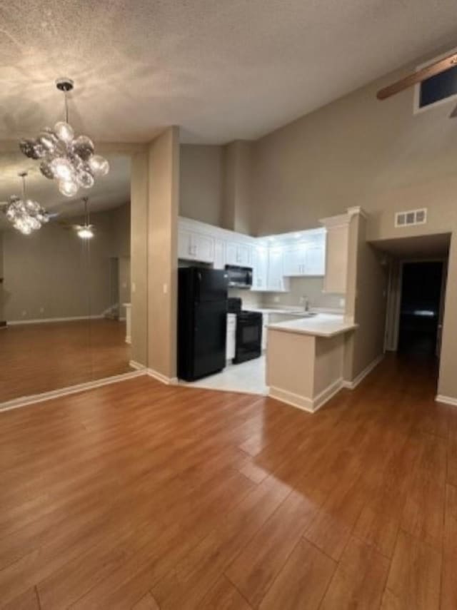 kitchen with white cabinetry, light hardwood / wood-style flooring, black refrigerator, kitchen peninsula, and stove