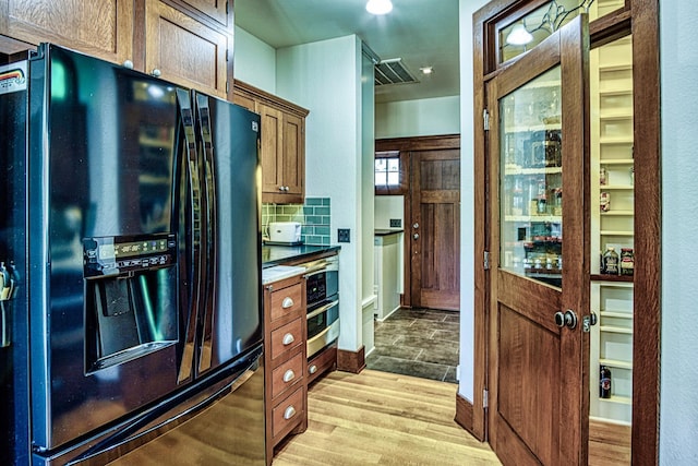 kitchen with light wood-type flooring, black fridge with ice dispenser, and decorative backsplash