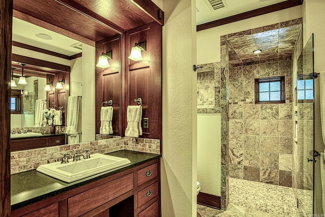 bathroom with tiled shower, vanity, ornamental molding, decorative backsplash, and toilet