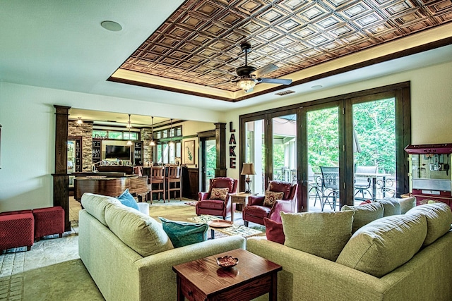 living room featuring decorative columns, a raised ceiling, ceiling fan, and french doors