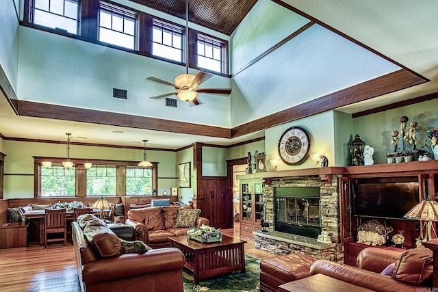 living room featuring crown molding, ceiling fan, a fireplace, hardwood / wood-style floors, and a high ceiling