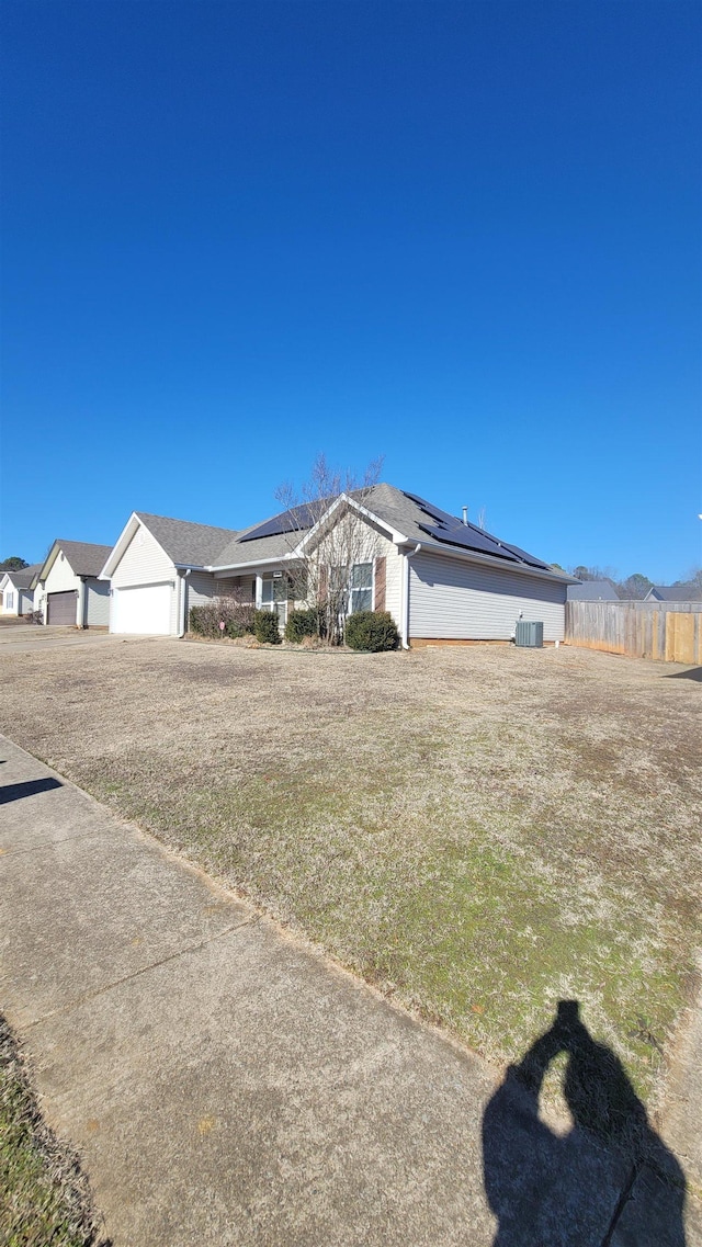 view of front of house with a garage, a front yard, central AC unit, and solar panels