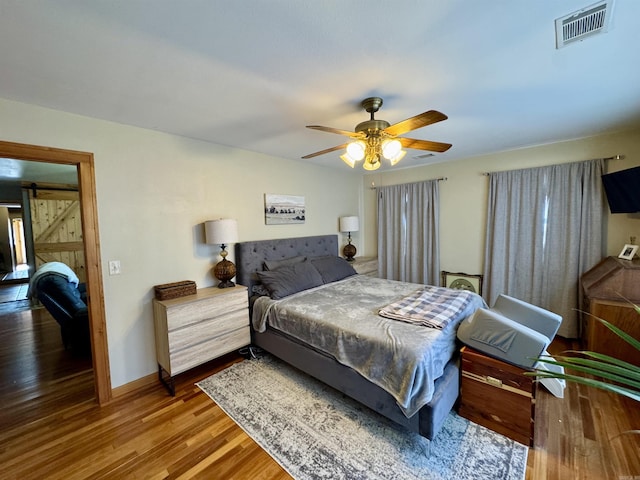 bedroom featuring a barn door, hardwood / wood-style floors, and ceiling fan