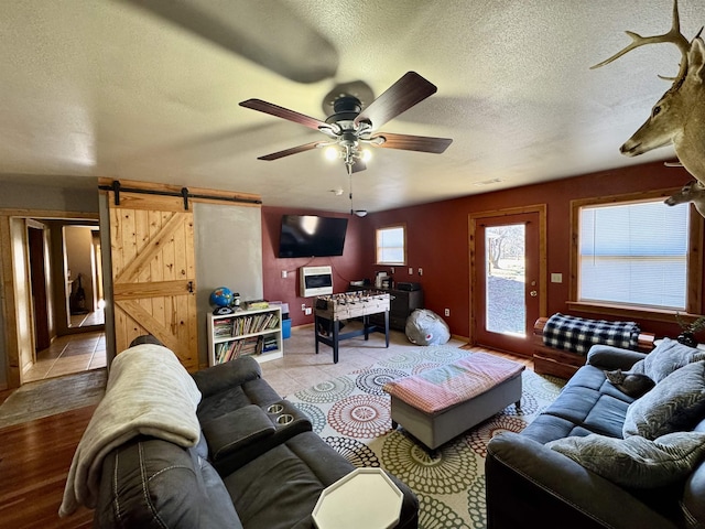 living room featuring a barn door, light wood-type flooring, a textured ceiling, and ceiling fan