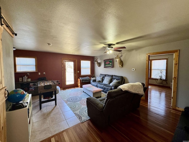 living room with ceiling fan, a barn door, a textured ceiling, and light wood-type flooring