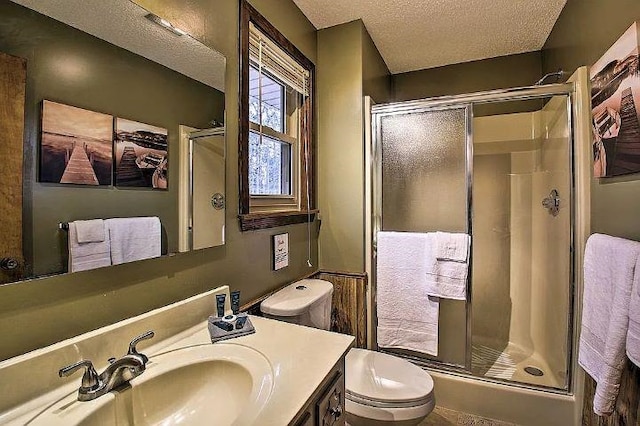 bathroom with vanity, a shower with door, toilet, and a textured ceiling