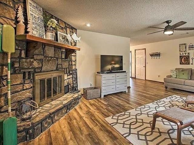 living room with a stone fireplace, wood-type flooring, and a textured ceiling