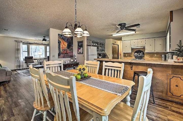 dining space featuring dark wood-type flooring, ceiling fan with notable chandelier, and a textured ceiling