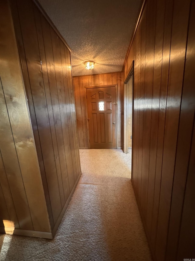 hallway featuring wooden walls, light carpet, and a textured ceiling