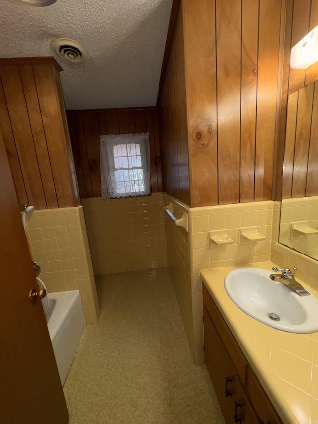 bathroom featuring wooden walls, tile walls, vanity, a washtub, and a textured ceiling