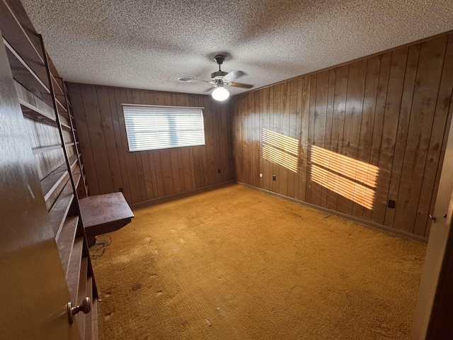 carpeted empty room with ceiling fan, a textured ceiling, and wooden walls