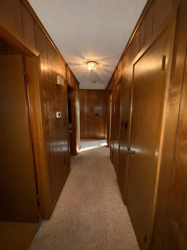 hallway featuring light carpet, a textured ceiling, and wood walls