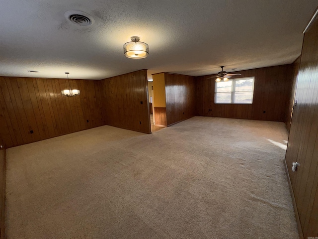 carpeted empty room with ceiling fan, a textured ceiling, and wood walls