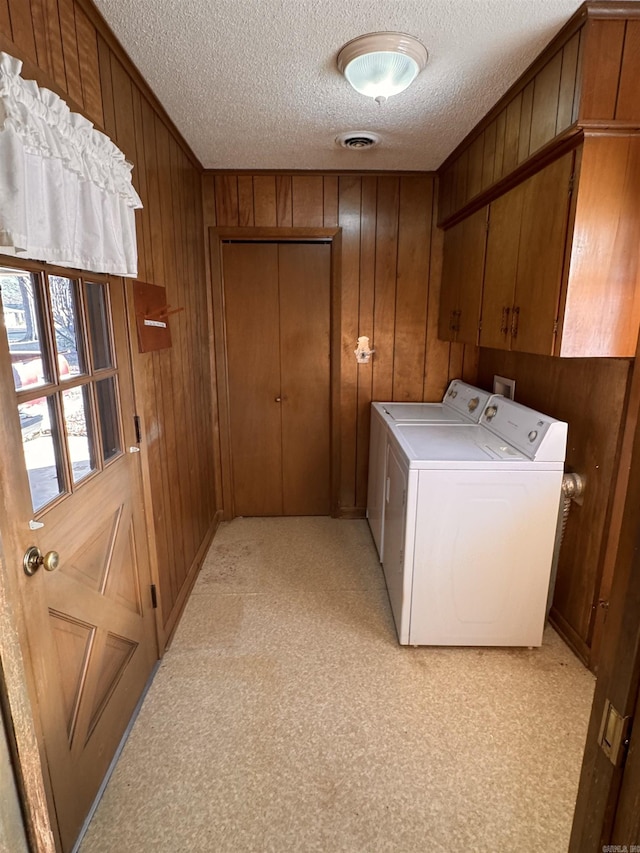 clothes washing area featuring cabinets, a textured ceiling, independent washer and dryer, and wood walls