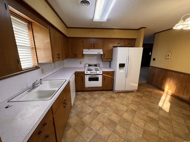 kitchen featuring wooden walls, sink, ornamental molding, white appliances, and a textured ceiling