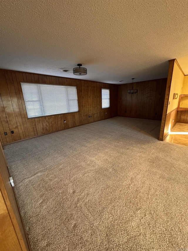 carpeted spare room with wooden walls and a textured ceiling