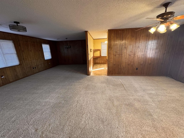 unfurnished room featuring light carpet, ceiling fan, a textured ceiling, and wood walls