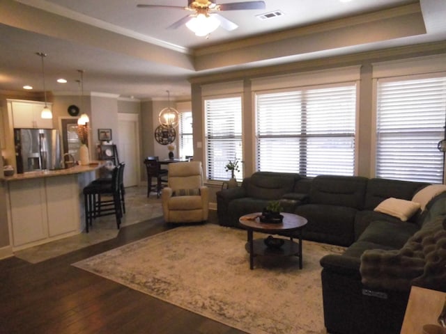 living room featuring wood-type flooring, ceiling fan with notable chandelier, crown molding, and a tray ceiling