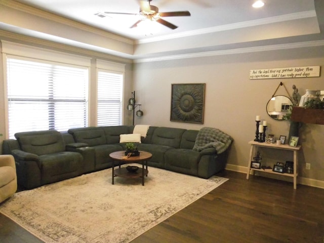 living room with a tray ceiling, dark wood-type flooring, ornamental molding, and ceiling fan