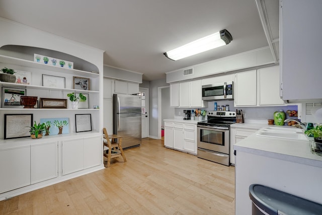 kitchen with sink, light hardwood / wood-style flooring, stainless steel appliances, ornamental molding, and white cabinets